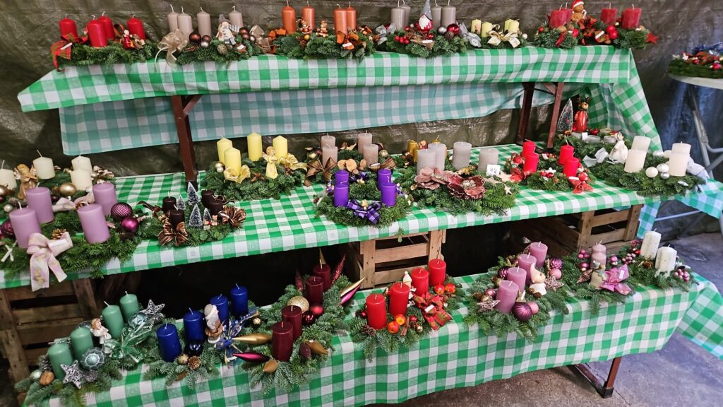 Auf drei übereinander gestellten Bierbänken werden bunte Adventskränze zum Verkauf angeboten.